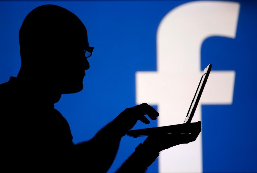 A man is silhouetted against a video screen with an Facebook logo as he poses with an Dell laptop in this photo illustration taken in the central Bosnian town of Zenica, August 14, 2013. REUTERS/Dado Ruvic (BOSNIA AND HERZEGOVINA - Tags: BUSINESS TELECOMS) - RTX12L6Y